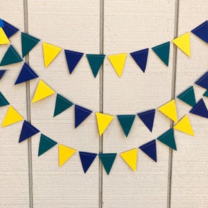 Peut inclure: Trois rang&eacute;es de fanions triangulaires jaunes, bleu marine et vert d'eau suspendues devant un fond en bois blanc. Les fanions sont espac&eacute;s de mani&egrave;re r&eacute;guli&egrave;re, cr&eacute;ant une d&eacute;coration festive. Les fanions sont faits d'un mat&eacute;riau robuste.