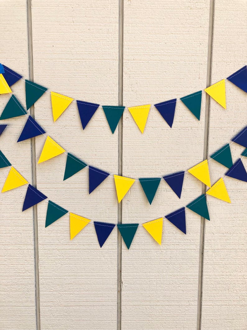 Peut inclure: Trois rang&eacute;es de fanions triangulaires jaunes, bleu marine et vert d'eau suspendues devant un fond en bois blanc. Les fanions sont espac&eacute;s de mani&egrave;re r&eacute;guli&egrave;re, cr&eacute;ant une d&eacute;coration festive. Les fanions sont faits d'un mat&eacute;riau robuste.