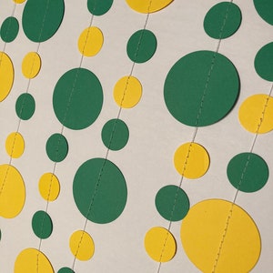 May include: A garland of alternating yellow and green paper circles strung together with white thread. The circles are different sizes and are sewn together with a decorative stitch.