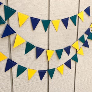 Peut inclure: Trois guirlandes de fanions triangulaires color&eacute;s jaunes, turquoise et bleu marine sont suspendues sur un fond en bois blanc. Les fanions sont espac&eacute;s uniform&eacute;ment et reli&eacute;s par un fil blanc, cr&eacute;ant une d&eacute;coration festive.