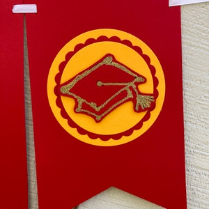 May include: Red and yellow graduation banner with a gold glitter graduation cap in the center.