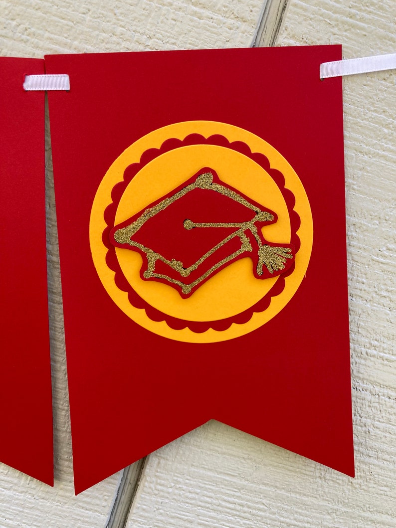 May include: Red and yellow graduation banner with a gold glitter graduation cap in the center.