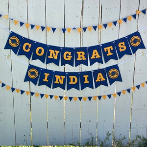 May include: A blue and gold graduation banner with the text "Congrats India" and a graduation cap icon on each end.
