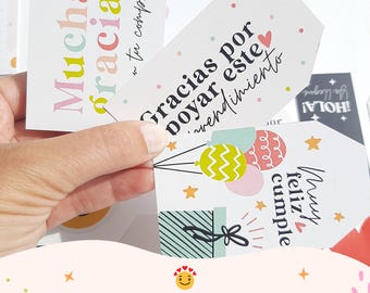 Könnte beinhalten: Eine Hand hält mehrere weiße Geschenkanhänger mit farbenfrohen Texten und Designs. Die Anhänger zeigen Sätze wie "Muchas gracias" und "Gracias por apoyar este emprendimiento." Der untere Teil des Bildes lautet "KIT IMPRIMIBLE PASTELES (EMPRENDEDORES)."