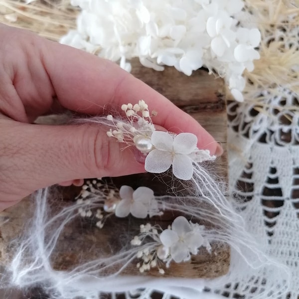 May include: White dried flowers with a pearl accent, arranged on a wooden surface with white lace fabric.