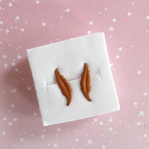 May include: A pair of brown feather-shaped earrings on a white display card.
