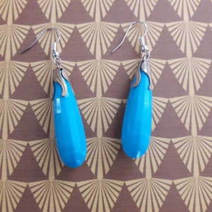 May include: A pair of dangle earrings with a teardrop-shaped blue stone and silver-toned metal accents.