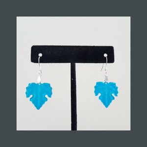 May include: A pair of turquoise blue leaf-shaped dangle earrings with silver hooks.