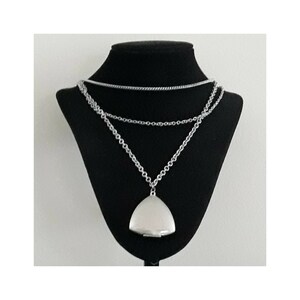 May include: A silver layered necklace with a triangular pendant. The pendant is a locket with a hinged lid.