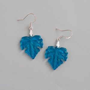 May include: A pair of silver dangle earrings with blue leaf-shaped charms. The leaves are translucent and have a textured surface.