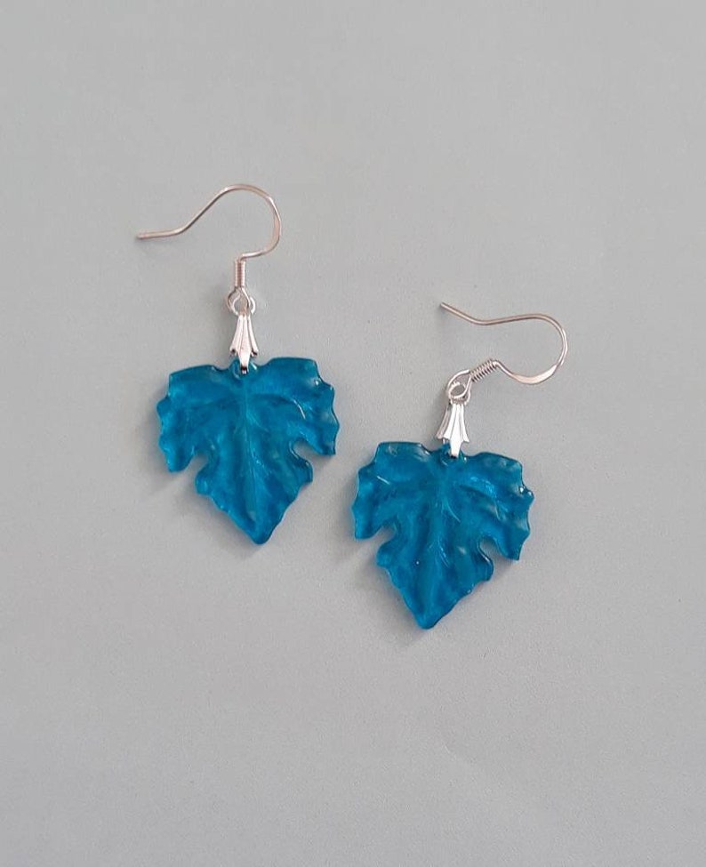 May include: A pair of silver dangle earrings with blue leaf-shaped charms. The leaves are translucent and have a textured surface.