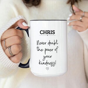 May include: White ceramic mug with a black handle and rim. The mug features the name "CHRIS" above the phrase "Never doubt the power of your kindness!" in black script. A small heart is at the bottom of the text.