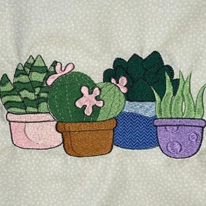 May include: Embroidered image of four potted succulents. The plants are green with pink accents, and the pots are in shades of pink, brown, blue, and purple. The background is a light beige fabric with small white polka dots.