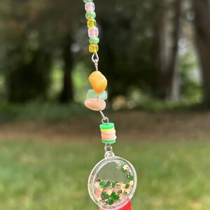 May include: A red and clear plastic gumball machine charm with green and gold glitter inside. The charm is attached to a silver chain with green, yellow, and pink beads.