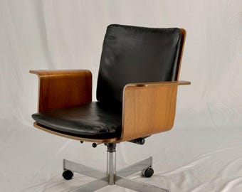 May include: An office chair with a black leather seat and backrest. The chair has wooden armrests and a wooden frame. The base is made of metal and has five wheels. The chair is designed for comfort and functionality.