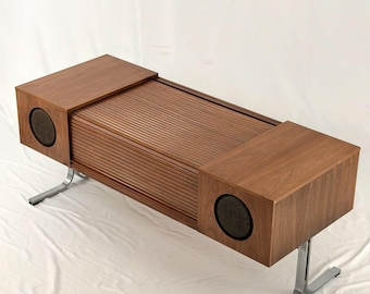 May include: A mid-century modern stereo console with a wooden cabinet and speakers on each end. The cabinet has a slatted front and sits on chrome legs. The speakers have dark mesh covers.