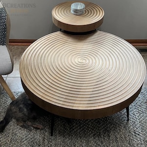 May include: Two-tiered wooden side tables with a spiral design. The larger table is at the bottom, with a smaller table above it. The tables have a light brown finish and black legs. A stack of coasters sits on the smaller table.