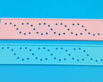 May include: Two rectangular, perforated plastic strips. One is light pink, the other is light blue. Both have a series of evenly spaced holes arranged in a wavy pattern. The background is a solid, bright blue.