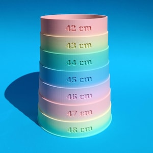 May include: A multi-colored, graduated cylinder with measurements from 42 cm to 48 cm. The cylinder is composed of stacked rings in shades of pink, yellow, green, blue, and purple. Each ring is labeled with its height in centimeters.