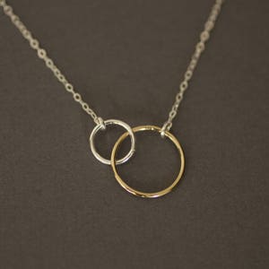 May include: A silver chain necklace with two interlocking circles, one silver and one gold.