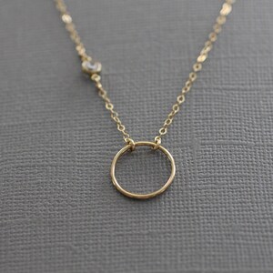 Puede incluir: Un collar de cadena de oro con un peque&ntilde;o colgante circular y un solo acento de piedra clara.