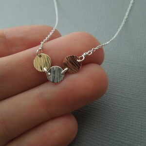 May include: A silver chain necklace with three textured metal discs. The discs are gold, silver, and copper.