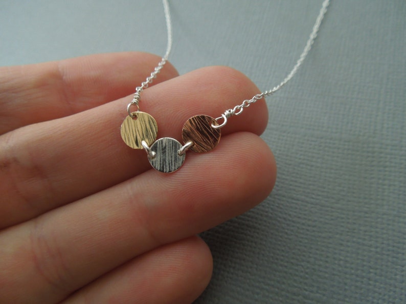 May include: A silver chain necklace with three textured metal discs. The discs are gold, silver, and copper.