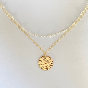 May include: A gold necklace with a hammered circle pendant and a silver chain.