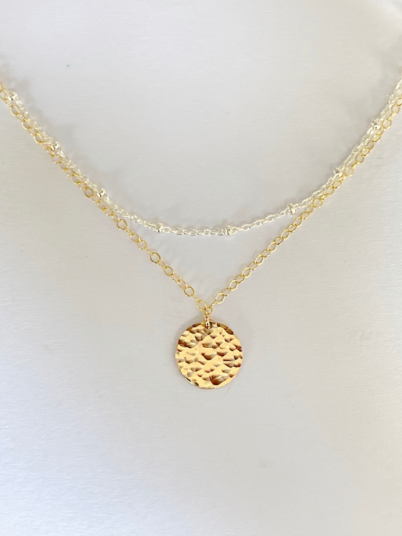 May include: A gold necklace with a hammered circle pendant and a silver chain.