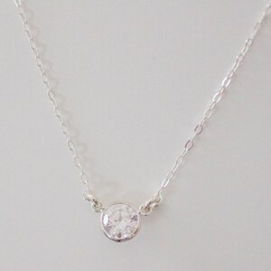 May include: A silver chain necklace with a single round clear crystal pendant.