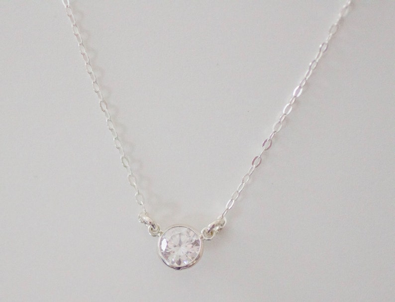 May include: A silver chain necklace with a single round clear crystal pendant.