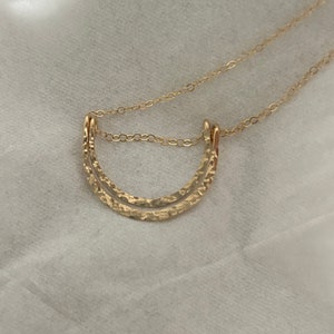 May include: A gold necklace with a double-layered, hammered crescent moon pendant.