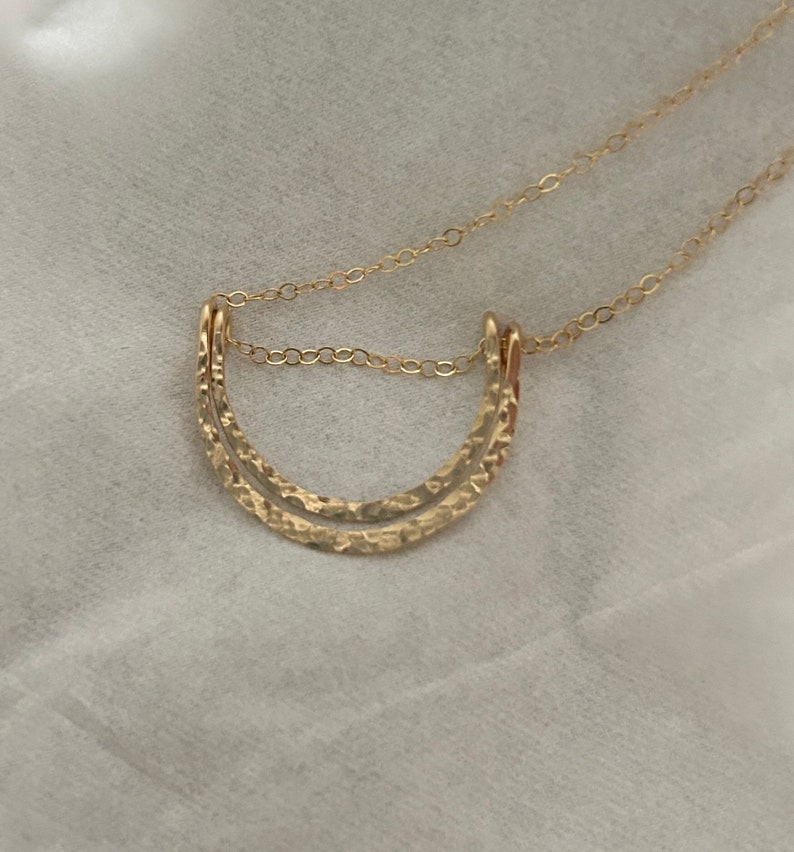 May include: A gold necklace with a double-layered, hammered crescent moon pendant.