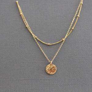 May include: A gold layered necklace with a hammered circle pendant.