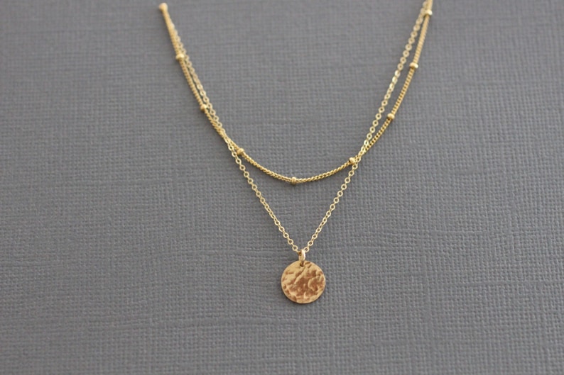May include: A gold layered necklace with a hammered circle pendant.