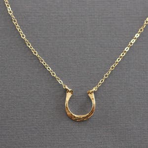 Peut inclure: Un collier en cha&icirc;ne dor&eacute;e avec un pendentif en forme de fer &agrave; cheval martel&eacute;.