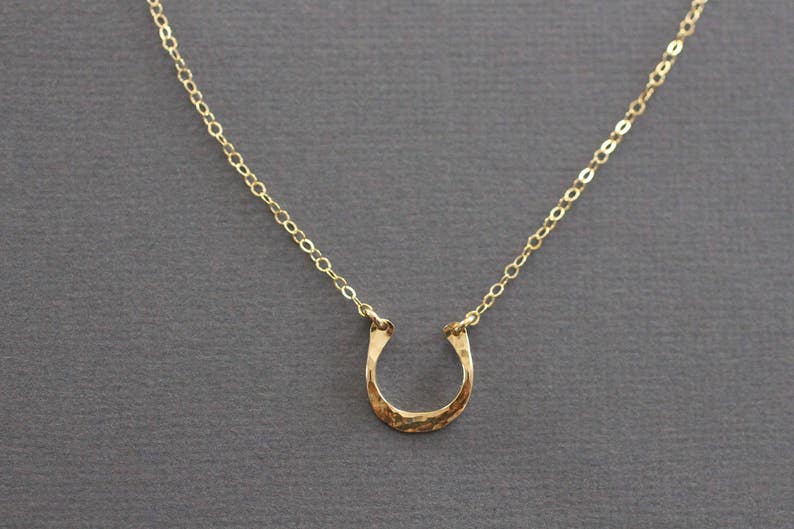 Peut inclure: Un collier en cha&icirc;ne dor&eacute;e avec un pendentif en forme de fer &agrave; cheval martel&eacute;.