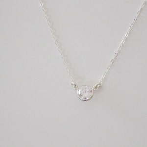 May include: A silver chain necklace with a single, clear, round gemstone pendant.