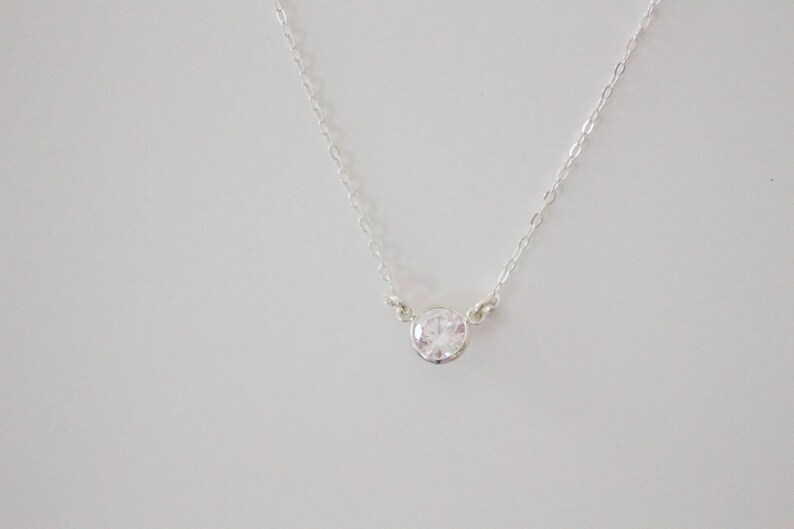 May include: A silver chain necklace with a single, clear, round gemstone pendant.