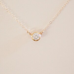 May include: A delicate gold chain necklace with a single, clear round gemstone pendant.