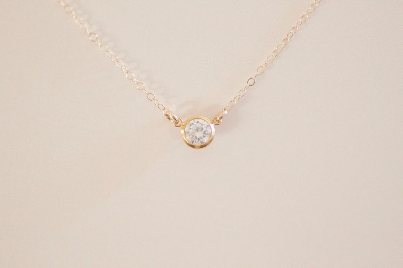 May include: A delicate gold chain necklace with a single, clear round gemstone pendant.