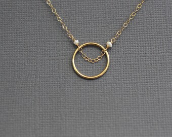 May include: A gold necklace with a circle pendant and two small white beads.