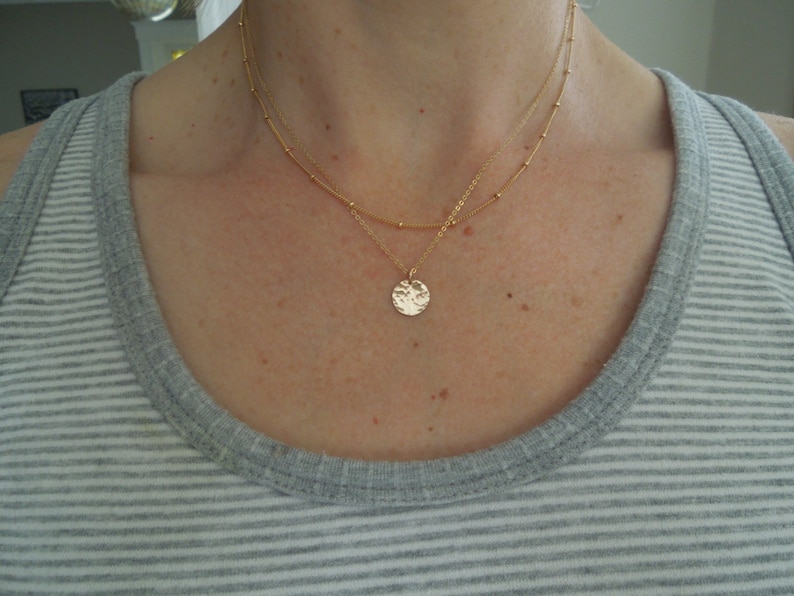 May include: A gold necklace with a delicate chain and a hammered circle pendant.
