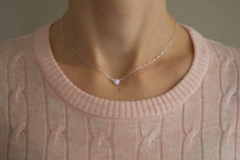 May include: A delicate silver chain necklace with a small, sparkly, round pendant.