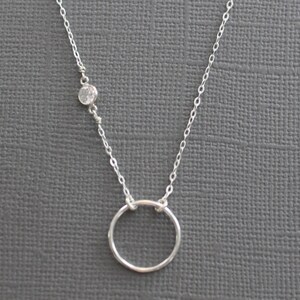 Puede incluir: Un collar de cadena de plata con un peque&ntilde;o acento de piedra clara y un colgante circular simple.