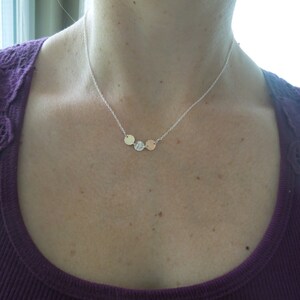 May include: A silver chain necklace with three small, round pendants. The pendants are silver, gold, and rose gold.