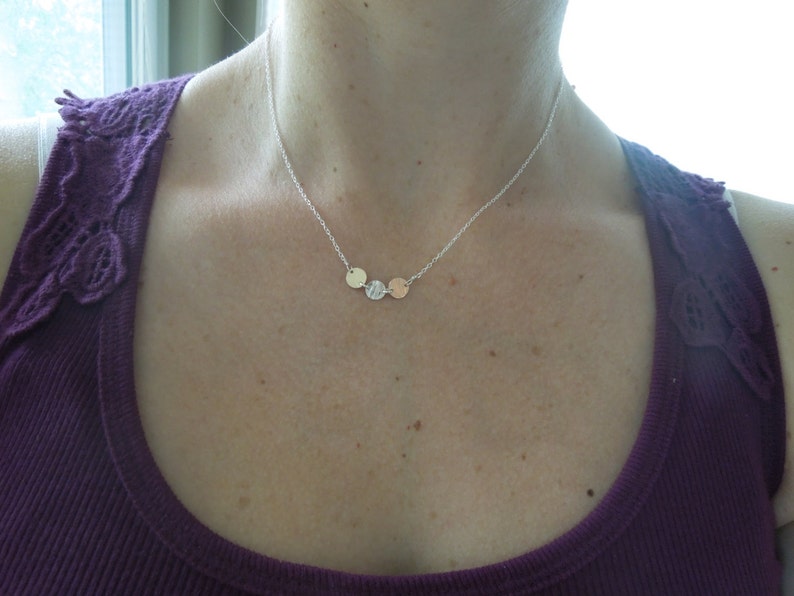 May include: A silver chain necklace with three small, round pendants. The pendants are silver, gold, and rose gold.