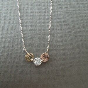 May include: A silver chain necklace with three round pendants. The pendants are made of different metals: gold, silver, and rose gold. Each pendant has a textured surface.