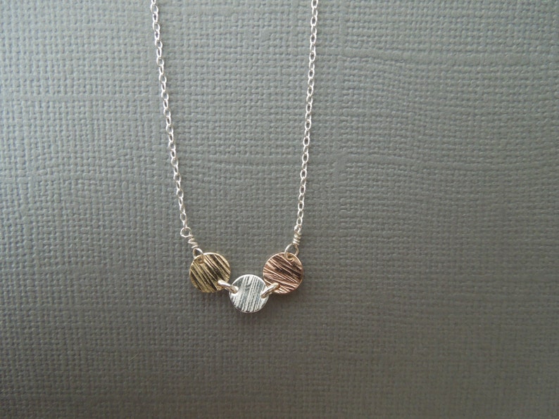 May include: A silver chain necklace with three round pendants. The pendants are made of different metals: gold, silver, and rose gold. Each pendant has a textured surface.