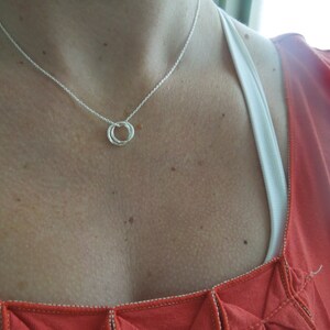 May include: A silver necklace with a simple, twisted circle pendant. The necklace is worn by a person with a red shirt.
